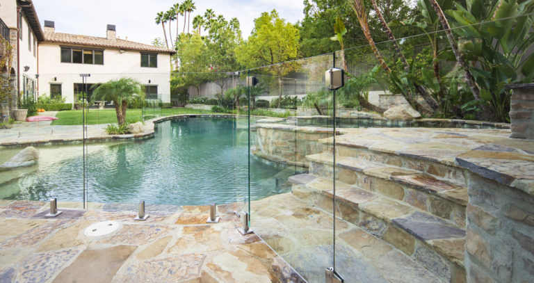 Glass pool gate attached to a glass fence in a luxurious back yard.