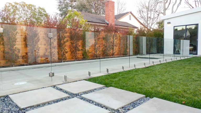 glass fence with a gate separating a pool from the front yard of a house.