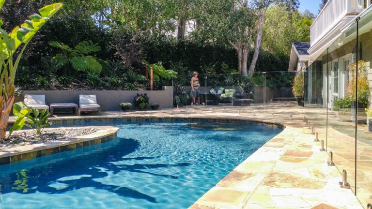 A homeowner stands behind her frameless glass pool fence surrounding her swimming pool.