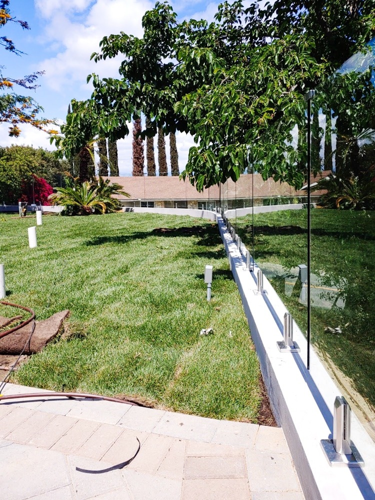 Frameless glass railing on a pony wall surround a back yard in a neighborhood