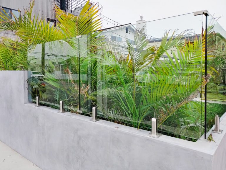 Small section of glass railing mounted to a pony wall surrounding plants and a backyard area