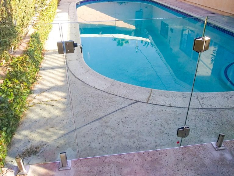 Frameless glass gate with lock and key in front of a swimming pool.