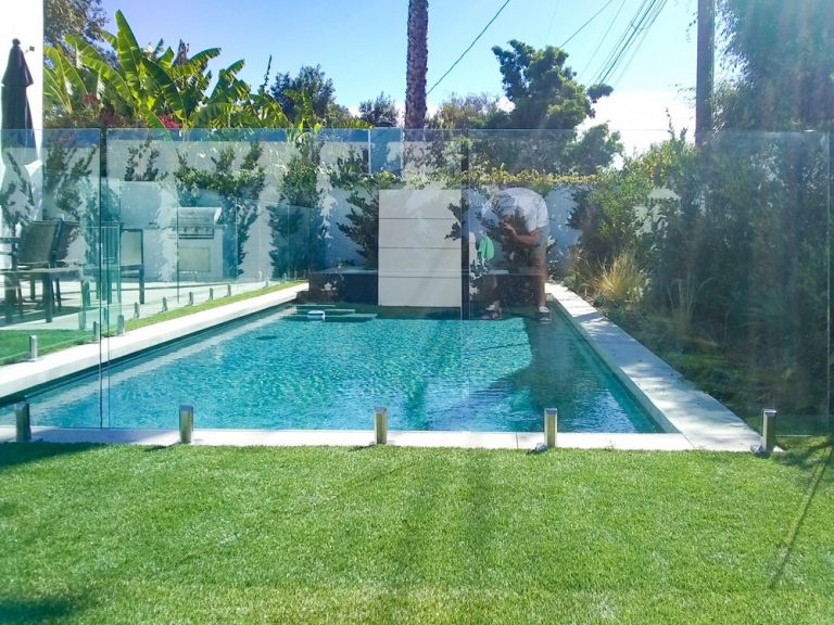 Glass pool fence with stainless steel spigots surrounding a backyard pool