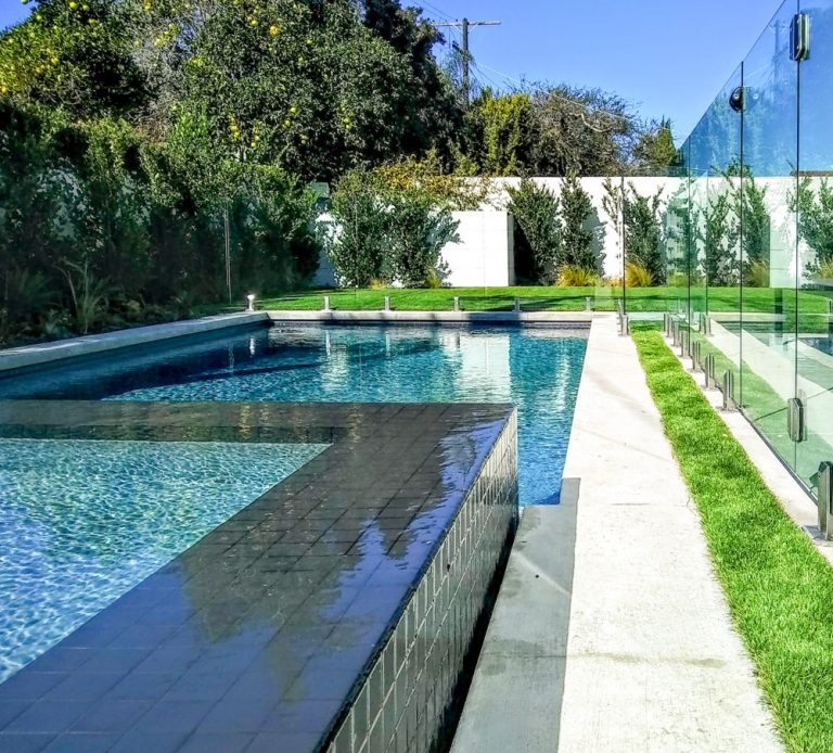 Glass pool fence with a gate surrounding a hot tub and swimming pool