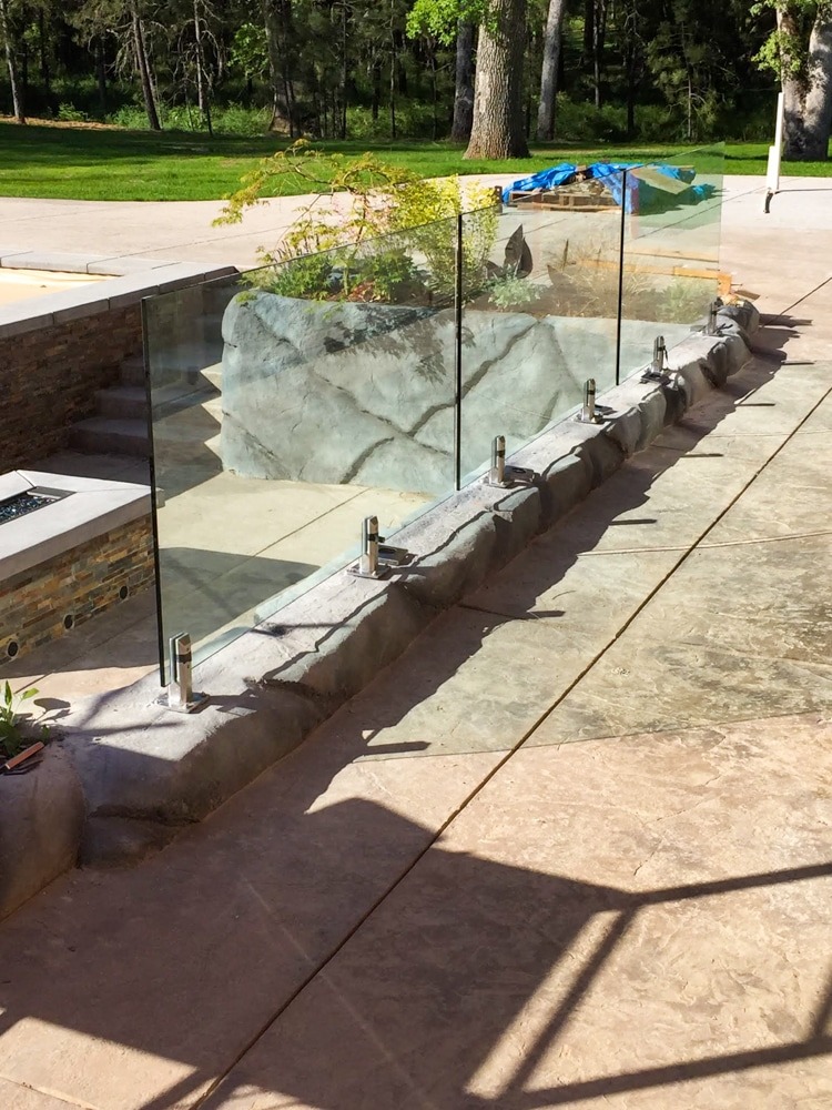 three panels of glass railing mounted to stone with stainless steel spigots