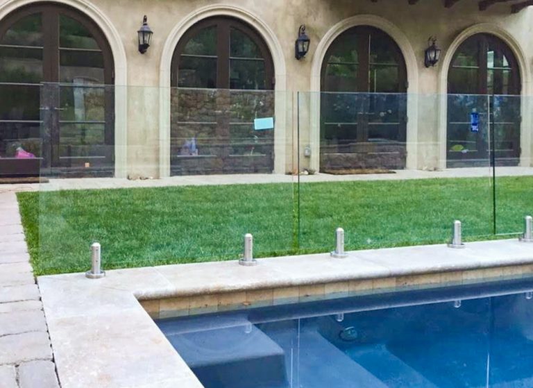 Glass pool fence surrounding a swimming pool in the backyard of a large home