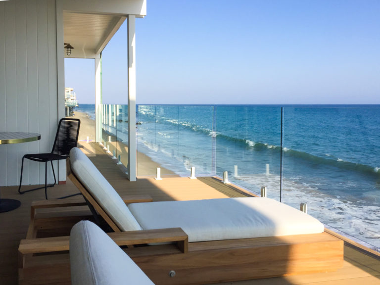 Glass railing with white spigots on a balcony overlooking the beach.