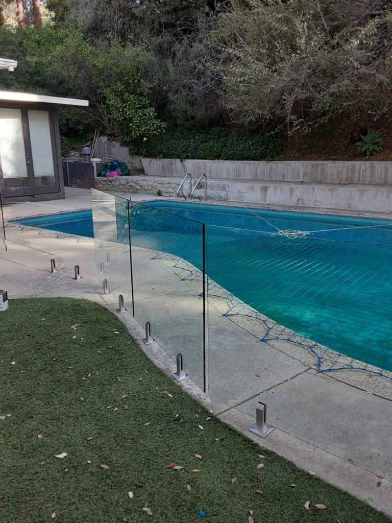 Glass pool fence in a back yard surrounding a swimming pool