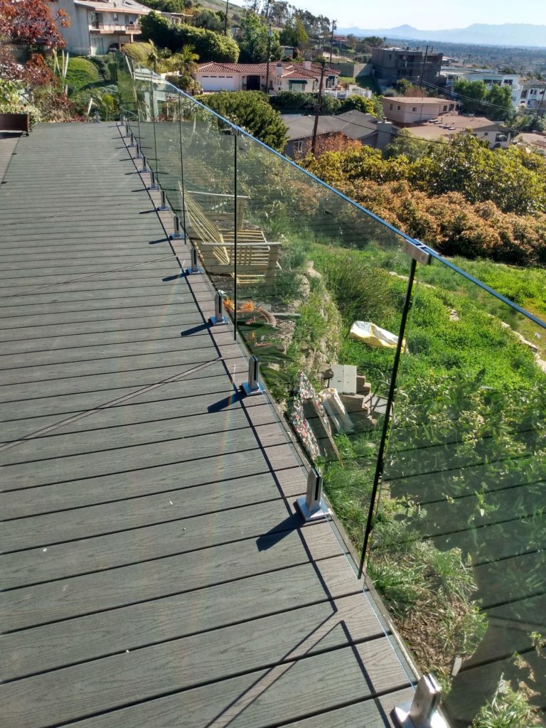Frameless glass railing with top clips on the second story of a wooden balcony.