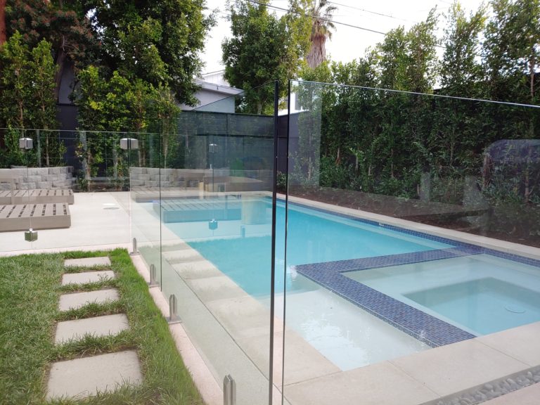 Glass fencing with stainless steel spigots surrounding a swimming pool in a back yard