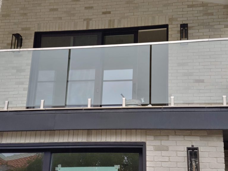 Glass railing with a top cap rail on an outdoor second story balcony connected to a house