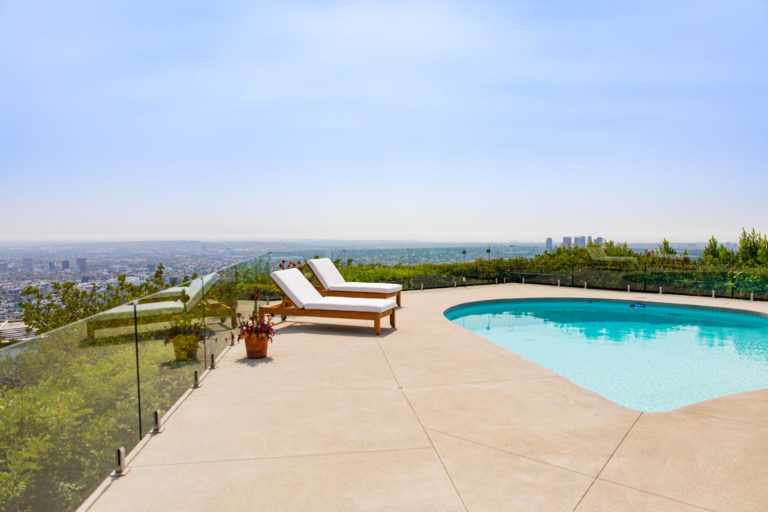 Frameless glass railing surrounding a concrete pool enclosure overlooking the Los Angeles skyline
