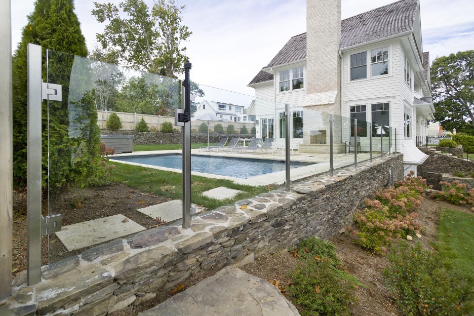 Semi frameless glass fencing with stainless steel posts surrounding a backyard with a pool